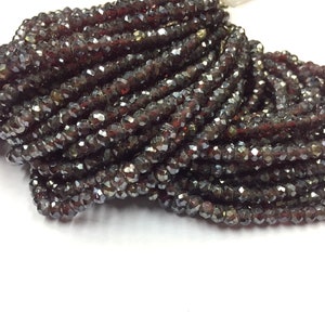 May include: A close-up of a pile of dark red faceted glass beads. The beads are small and have a shiny finish.