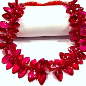 May include: A strand of bright red marquise-shaped gemstone beads. The beads are strung on a clear thread and are ready to be used for jewelry making.