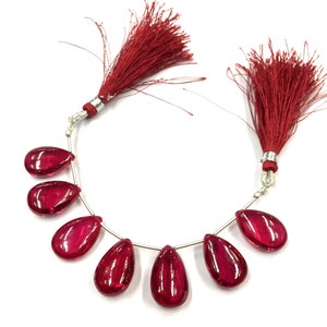 May include: A strand of seven red gemstone beads, each shaped like a teardrop, strung on a silver wire with red tassels at each end.