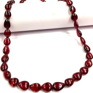 Puede incluir: Una hebra de cuentas de piedras preciosas de color rojo intenso en forma de lágrima. Las cuentas están enhebradas en un hilo transparente y están dispuestas en un diseño simple y elegante.