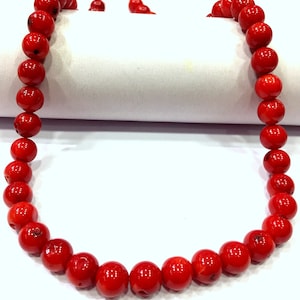 Op de afbeelding: Een streng helderrode koraal kralen, geregen tot een ketting. De kralen zijn rond en glad, met een natuurlijke, gepolijste afwerking.