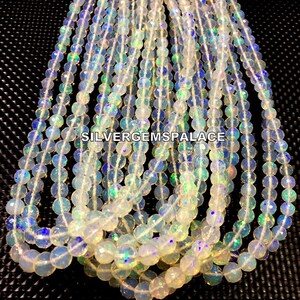 May include: A strand of white opal beads with iridescent rainbow flashes. The beads are round and have a smooth, polished finish. The strand is approximately 16 inches long and is perfect for making jewelry.