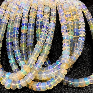 May include: A strand of white opal beads with iridescent rainbow flashes. The beads are round and have a smooth, polished finish. The strand is approximately 40 cm long.