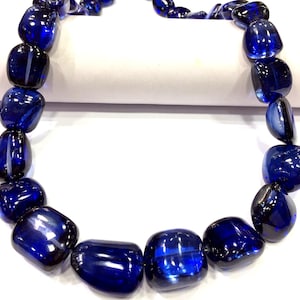 May include: A strand of deep blue gemstone beads, each bead is a smooth, rounded, and slightly elongated oval shape.