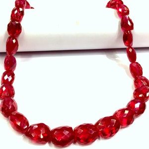 May include: A strand of deep red faceted gemstone beads. The beads are oval shaped and have a polished finish.