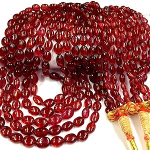 Puede incluir: Una hebra de cuentas de rubí rojo, de forma ovalada, con borlas doradas en el extremo.