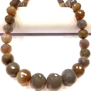 May include: A strand of brown and gray faceted gemstone beads. The beads are round and have a smooth, polished finish.