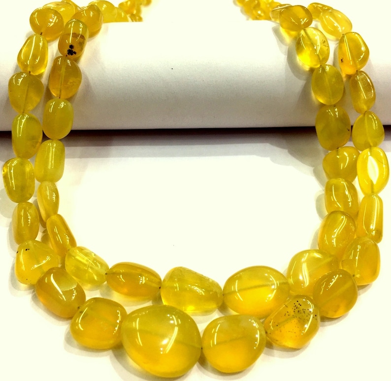 May include: A strand of yellow gemstone beads, likely opal, in a teardrop shape. The beads are strung on a clear thread and are arranged in a double row.