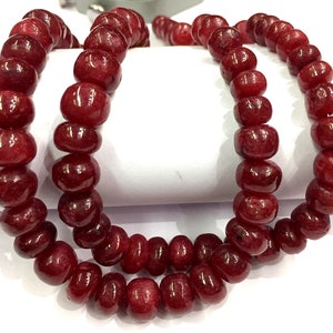 May include: A strand of deep red gemstone beads. The beads are round and have a smooth, polished finish.