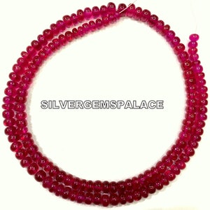 Op de afbeelding: Een streng van felroze robijn kralen, elke kraal is rond en glad. De kralen zijn geregen aan een wit draad en zijn gerangschikt in een cirkel. De tekst "SILVERGEMSPALACE" is zichtbaar in het midden van de afbeelding.