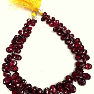 May include: A strand of deep red gemstone beads, likely garnet, with a yellow tassel at the end. The beads are faceted and have a teardrop shape.