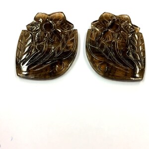 May include: Two carved smoky quartz pendants in the shape of a flower with leaves. The pendants are a dark brown color and have a glossy finish.