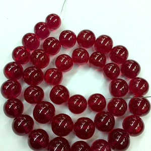 以下が含まれることがあります： 深紅色のガラスビーズのネックレス。ビーズは丸くて滑らかで、細いワイヤーに糸で通され、円形に配置されています。