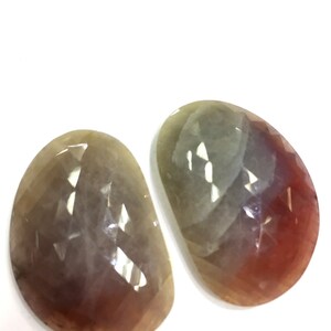 May include: Two faceted gemstone cabochons with a gradient of colors, including gray, pink, and brown.
