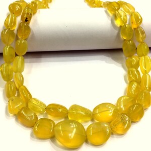 May include: A double strand necklace made of yellow opal gemstone beads. The beads are smooth and oval shaped.