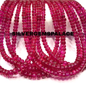 Puede incluir: Múltiples hilos de cuentas redondas de color rosa fucsia vibrante dispuestos en una serie de bucles. Las cuentas tienen una calidad translúcida y un acabado suave y pulido. El texto SILVERGEMSPALACE está impreso en negro sobre los hilos.