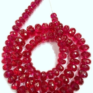 May include: A strand of deep red faceted gemstone beads. The beads are round and have a polished finish. The beads are strung on a thin wire.