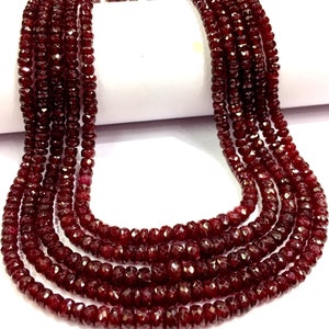 May include: A strand of deep red ruby beads, faceted and polished, strung together in a long necklace. The beads are arranged in a loose, flowing pattern, creating a luxurious and elegant look.