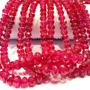 May include: A strand of red faceted gemstone beads. The beads are round and have a shiny finish. The beads are strung on a clear thread. The strand is approximately 16 inches long. SILVERGEMSPALACE is printed on the white surface.