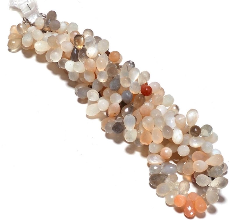 May include: A strand of light gray, peach, and white moonstone beads. The beads are teardrop shaped and have a pearlescent sheen.