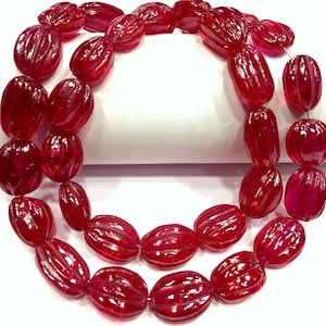 May include: A strand of red ruby beads with a faceted, oval shape. The beads have a textured, ribbed surface.