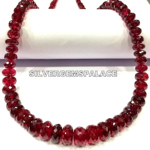 Puede incluir: Una hebra de cuentas de piedras preciosas facetadas de color rojo intenso. Las cuentas están enhebradas en un hilo transparente y tienen aproximadamente 6 mm de diámetro. Las cuentas están dispuestas en un patrón circular, formando un collar.