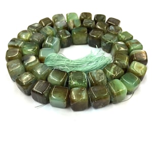 Può includere: Una collana di perle di pietre preziose verdi e marroni, ogni perla ha una forma quadrata con bordi arrotondati. Le perle sono infilate su un filo sottile e hanno un fiocco verde all'estremità.