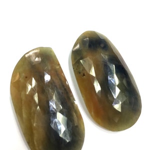 Puede incluir: Dos piedras preciosas de forma ovalada con un corte facetado. Las piedras son una mezcla de colores marrón, amarillo y azul.