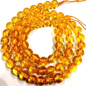 Peut inclure: Un brin de perles rondes, translucides et jaunes avec des paillettes dor&eacute;es. Les perles sont enfil&eacute;es sur un cordon orange fin.