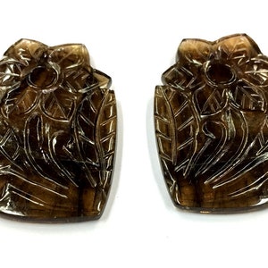 May include: Two brown carved gemstone pendants in the shape of a flower with leaves. The pendants are intricately carved with a floral design.