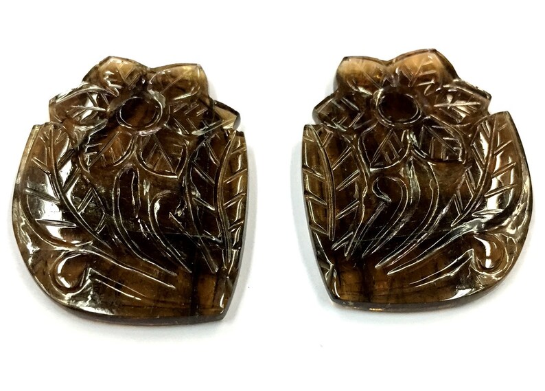 May include: Two brown carved gemstone pendants in the shape of a flower with leaves. The pendants are intricately carved with a floral design.