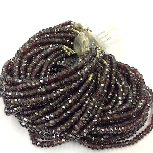 May include: A large strand of dark red faceted glass beads. The beads are small and uniform in size and shape. The strand is coiled and ready for use in jewelry making.