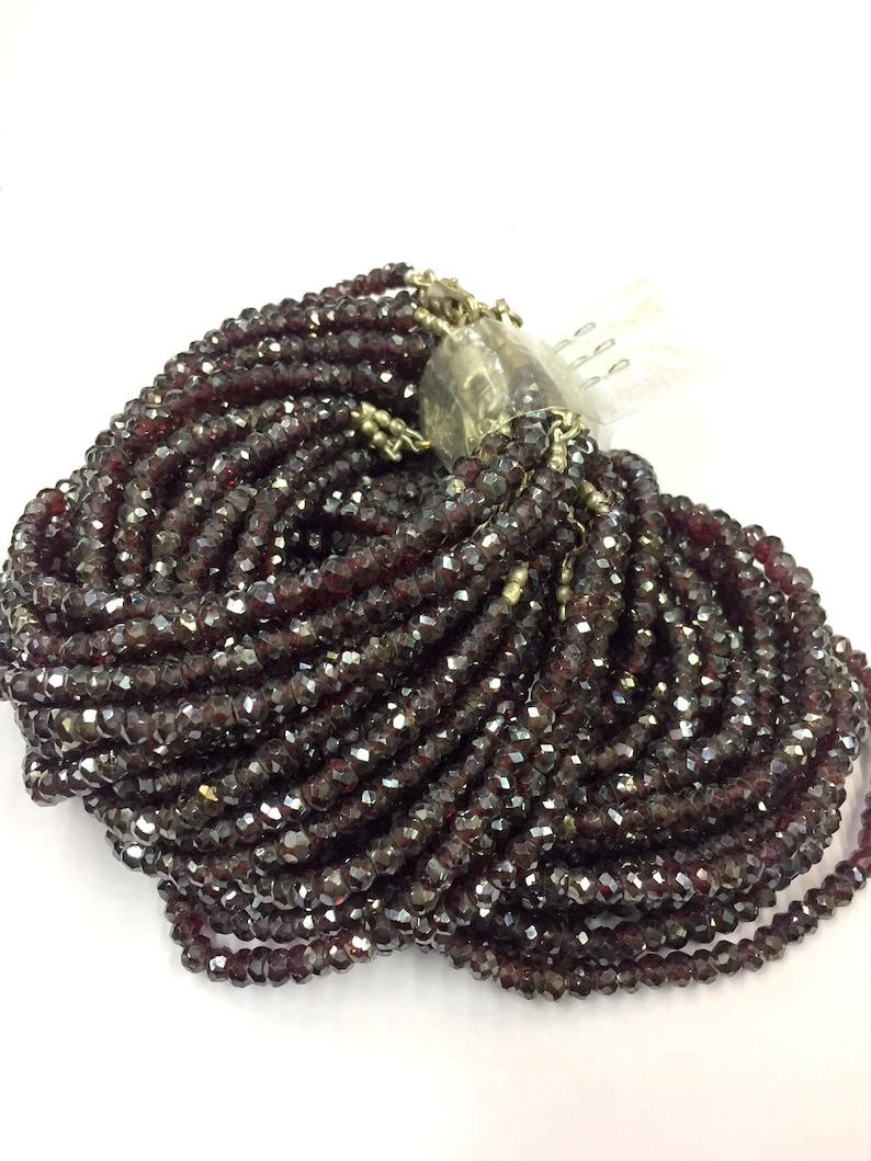 May include: A large strand of dark red faceted glass beads. The beads are small and uniform in size and shape. The strand is coiled and ready for use in jewelry making.