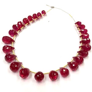 May include: A strand of red gemstone beads in a teardrop shape. The beads are strung on a gold wire.