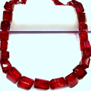 May include: A strand of deep red faceted gemstone beads. The beads are rectangular in shape and have a glossy finish.