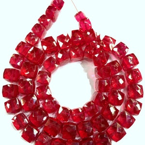 May include: A strand of red faceted gemstone beads. The beads are square shaped and have a glossy finish.