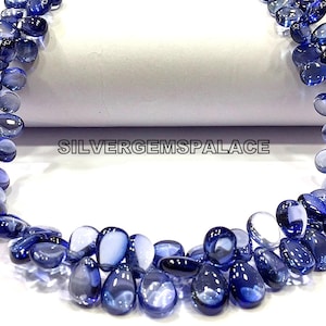May include: A strand of blue gemstone beads, each bead is a teardrop shape with a light blue to dark blue gradient. The beads are strung on a clear thread and are arranged in a loose, flowing pattern. The beads are displayed on a white surface with the text "SILVERGEMSPALACE" printed on the surface.