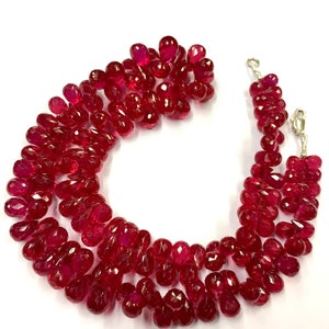 Puede incluir: Una hebra de cuentas de piedras preciosas facetadas de color rojo rubí, enhebradas en una cadena de plata con cierres de langosta. Las cuentas son de forma de pera y tienen un acabado pulido.