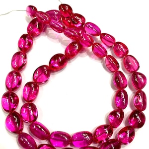 May include: A strand of pink oval-shaped beads. The beads are translucent and have a glossy finish.