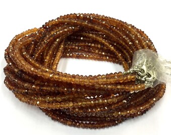 May include: A strand of brown gemstone beads, likely garnet, with a silver clasp. The beads are faceted and have a shiny finish.