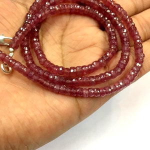 Op de afbeelding: Een streng facetgeslepen robijn kralen, geregen op een zilveren ketting. De kralen zijn diep rood van kleur en hebben een licht onregelmatige vorm.