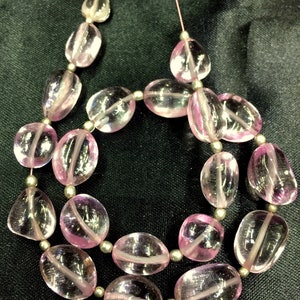 Puede incluir: Un collar de cuentas de piedras preciosas ovaladas de color rosa, enhebradas en un alambre plateado. Las cuentas son translúcidas y tienen un ligero brillo.