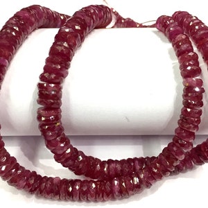 May include: A strand of deep red ruby beads, faceted and polished, strung on a thin thread. The beads are arranged in a circular pattern, creating a necklace or bracelet.