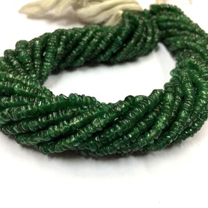 May include: A strand of dark green jade beads, each bead is faceted and has a slightly irregular shape. The beads are strung on a white thread and are ready to be used for jewelry making.