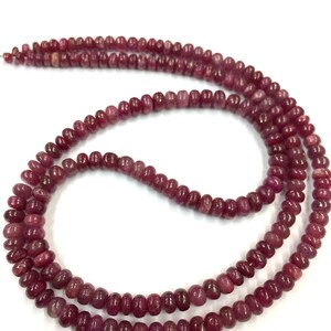 Puede incluir: Una hebra de cuentas de rubí rojo oscuro, enhebradas en un hilo transparente. Las cuentas son redondas y lisas, con una ligera variación de tamaño. La hebra es lo suficientemente larga como para usarse como collar o pulsera.