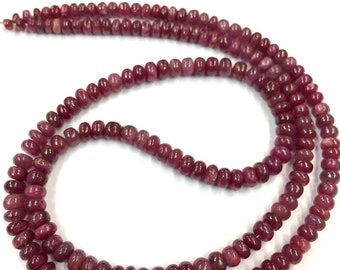 May include: A strand of deep red ruby beads, strung on a clear thread. The beads are round and smooth, with a slight variation in size. The strand is long enough to be worn as a necklace or bracelet.
