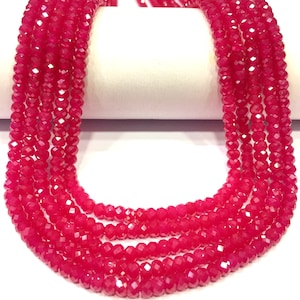 Op de afbeelding: Een streng helder roze facetgeslepen edelsteen kralen. De kralen zijn klein en rond en zijn geregen op een doorzichtige draad. De kralen zijn gerangschikt in een los, vloeiend patroon.