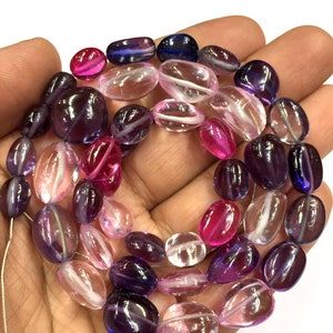 Puede incluir: Una hebra de cuentas de piedras preciosas de forma ovalada en tonos rosa, morado y transparente. Las cuentas son translúcidas y tienen un ligero brillo.