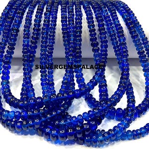 Könnte beinhalten: Eine Strähne aus blauen Glasperlen mit glatter, runder Form. Die Perlen sind auf einem durchsichtigen Faden aufgereiht, und die Strähne ist lang genug, um als Halskette oder Armband getragen zu werden.