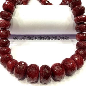 May include: A strand of deep red ruby beads, each bead is faceted and has a rounded shape. The beads are strung together to form a necklace.